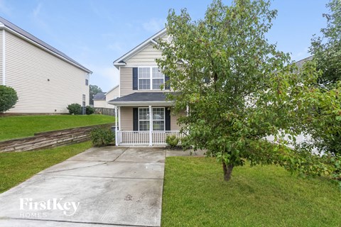 a small house with a sidewalk and a tree in front of it