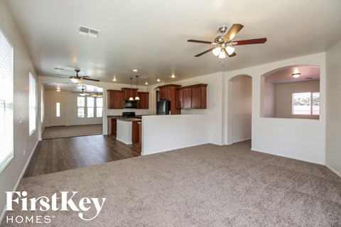 A spacious living room with a kitchen in the background and a carpet on the floor.