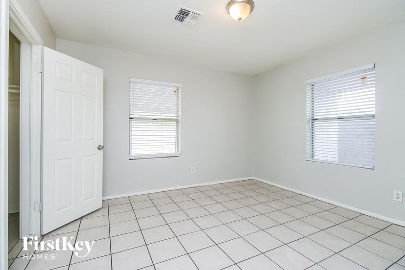 A white room with a door, a window with blinds, and a tiled floor.