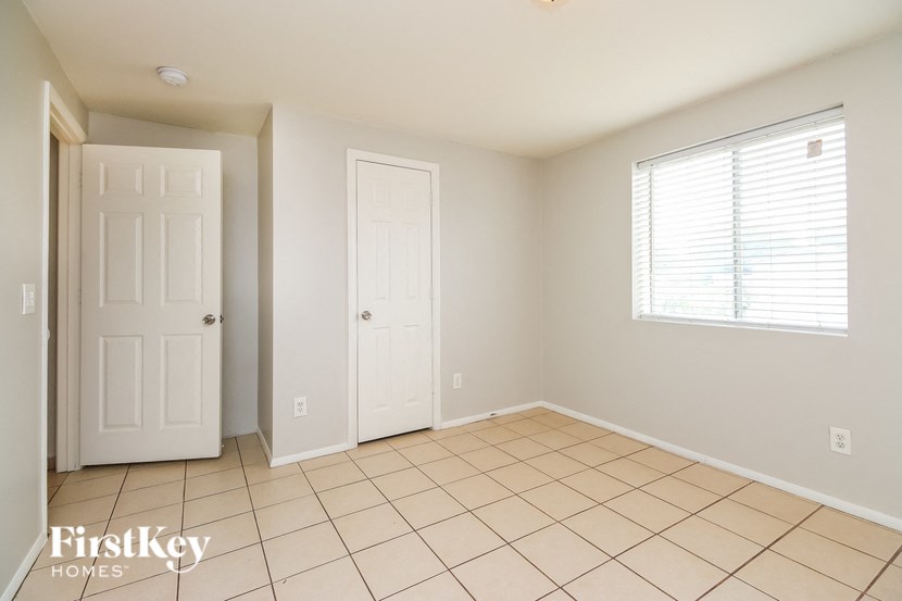 A room with a white door, a window with blinds, and a tiled floor.