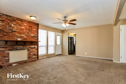 A spacious room with a brick fireplace and a ceiling fan.