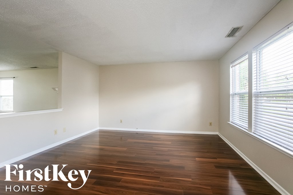 A room with wooden floors and white walls, with a window on the right side.
