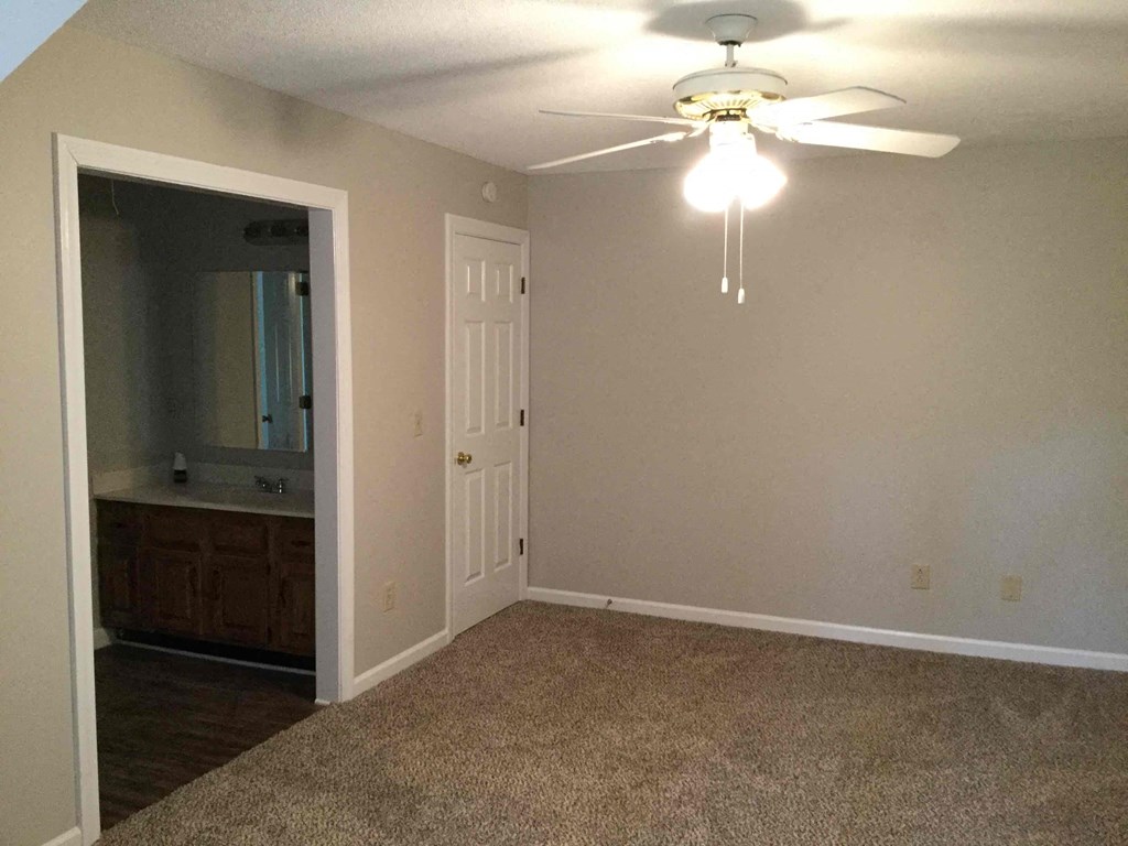 a empty living room with a ceiling fan and a door to the bathroom