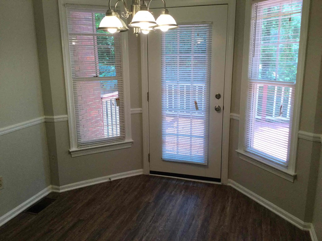 a door into a room with a wood floor and three windows