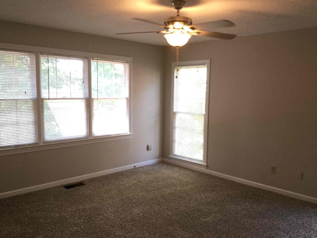 an empty living room with a ceiling fan and three windows