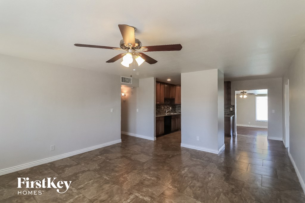 an empty living room with a ceiling fan and a kitchen