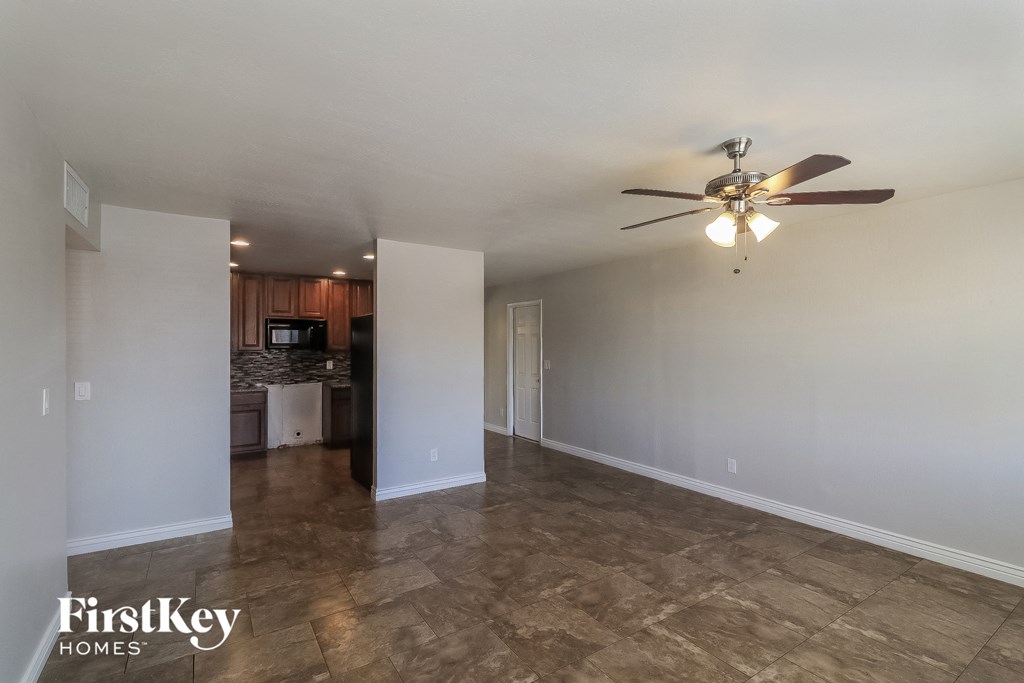 an empty living room with a ceiling fan and a kitchen