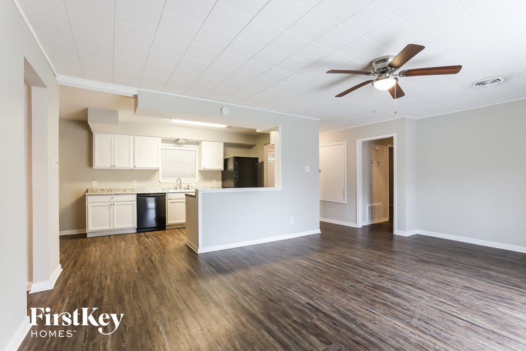 an empty living room and kitchen with wood flooring and a ceiling fan