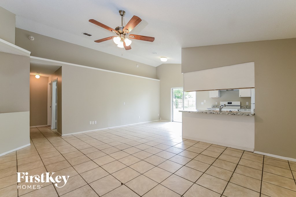 an empty living room with a ceiling fan and a kitchen
