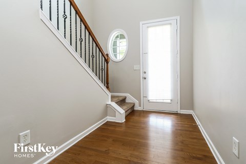 a foyer with a staircase and a door to a room with wood floors