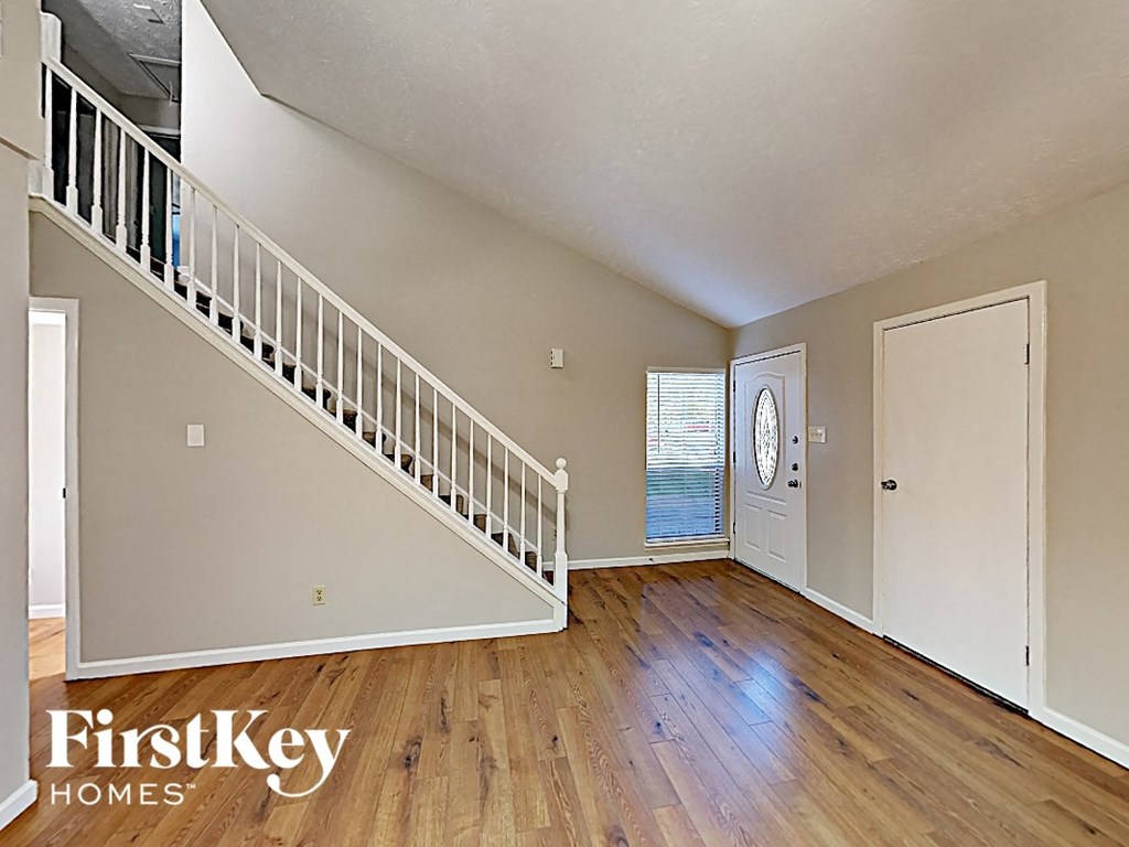 the living room and entryway of a house with wood floors and a staircase