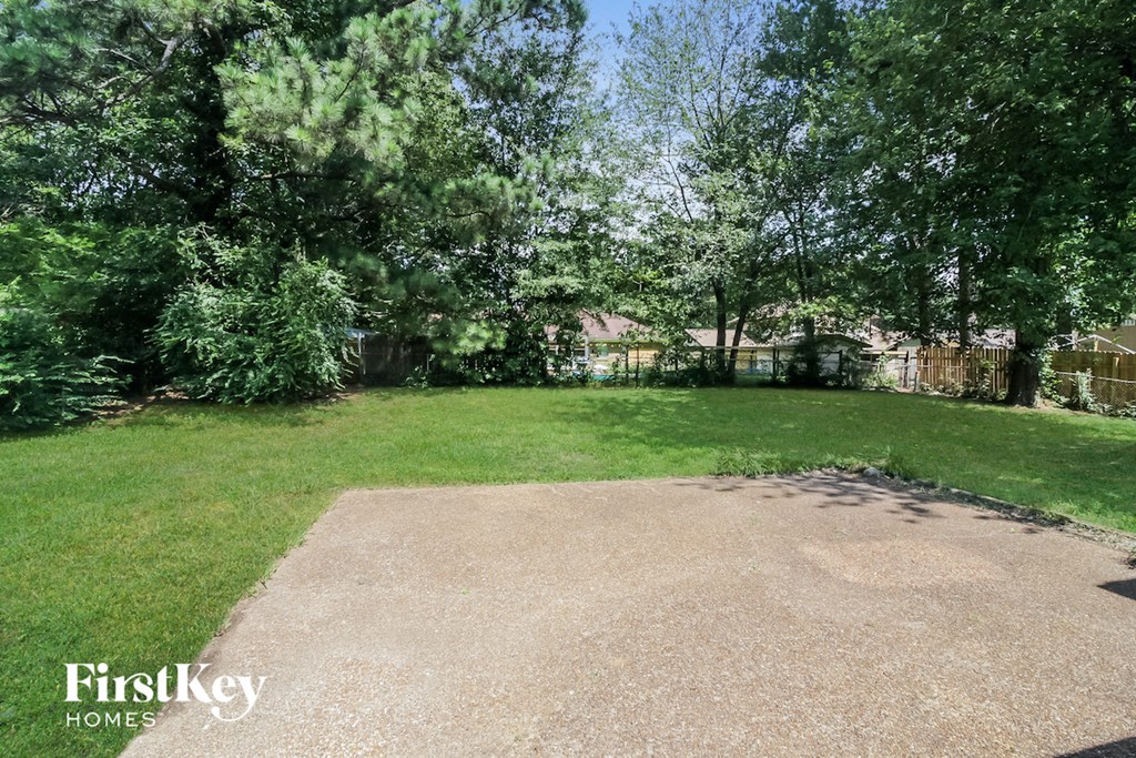 a backyard with a gravel driveway and green grass and trees