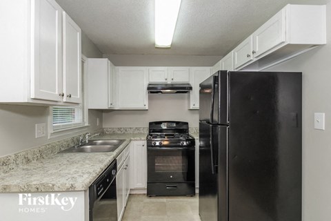 A kitchen with a black refrigerator and white cabinets.