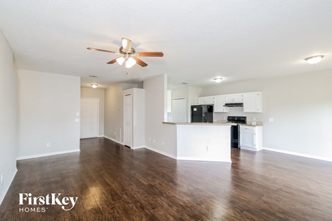 an empty living room with a ceiling fan and a kitchen