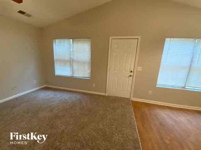A room with a carpeted floor, a door, and two windows.