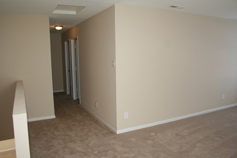 a living room with a carpeted floor and a hallway with a door open