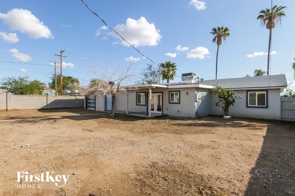 a small white house with a dirt lot and palm trees