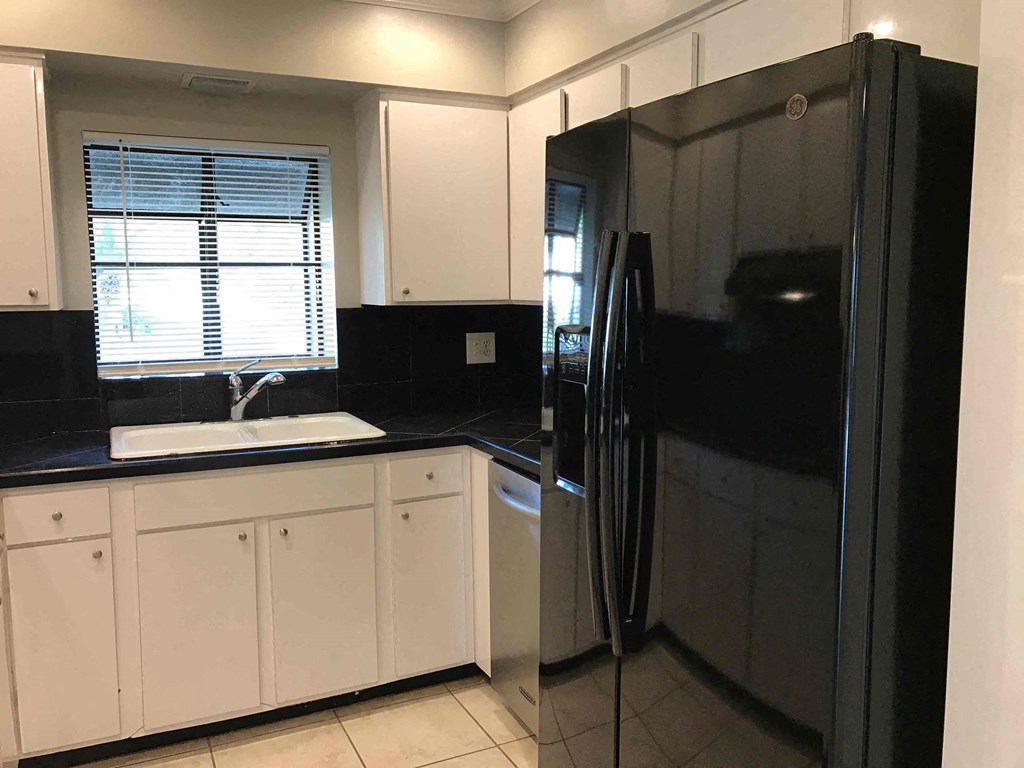 A black refrigerator stands in a kitchen with white cabinets and a black countertop.
