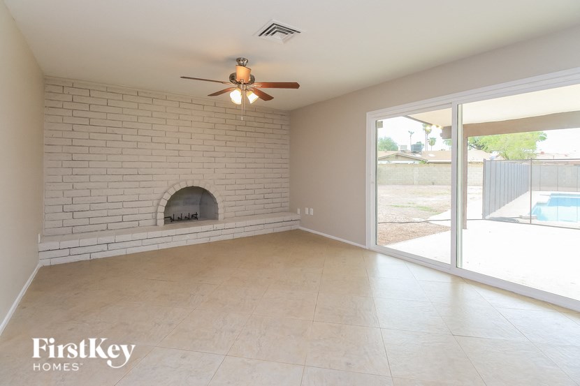 an empty living room with a brick fireplace and a ceiling fan