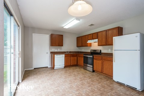A kitchen with a white refrigerator, brown cabinets, and a tiled floor.
