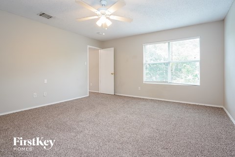 A room with a carpet floor, a ceiling fan, and a window with a view of trees.