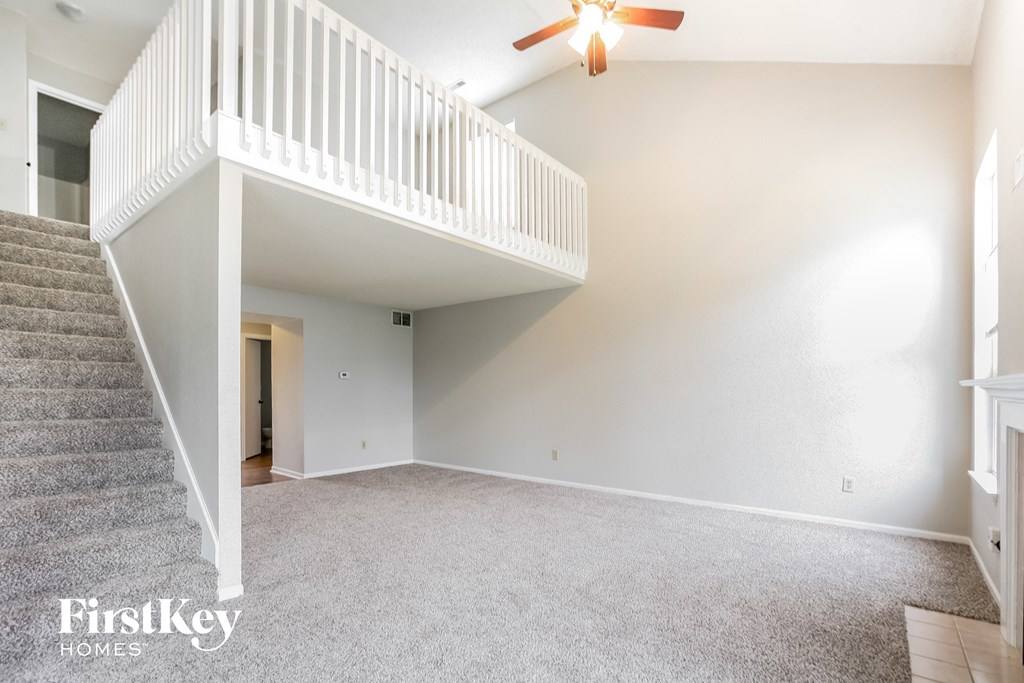 an empty living room with a ceiling fan and a staircase