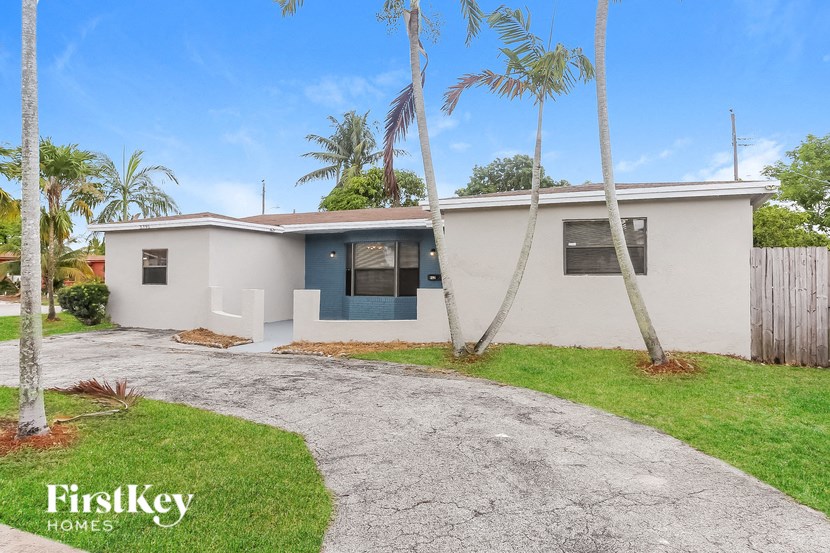 A house with a driveway and palm trees in front.