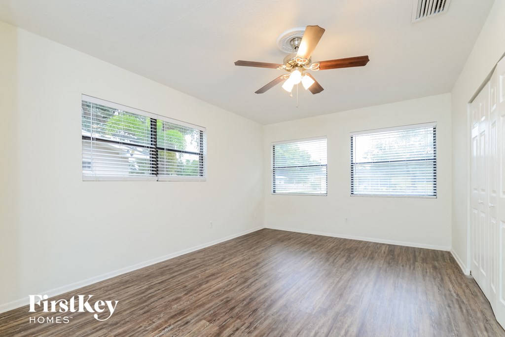 A room with a ceiling fan and three windows.