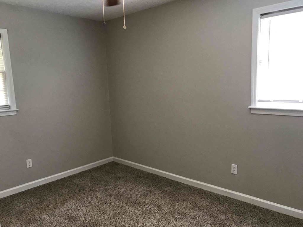 a room with gray walls and a carpet and two windows