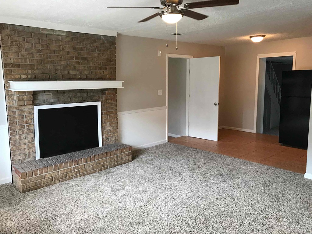 an empty living room with a brick fireplace and a ceiling fan