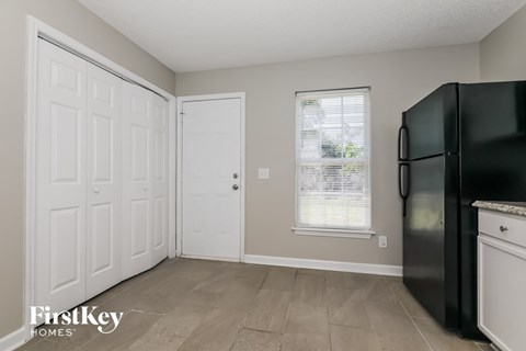 A black fridge sits in a kitchen with a white door and a window.