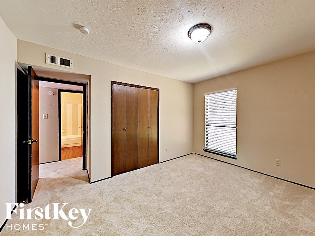 A bedroom with a carpeted floor and a window with blinds.