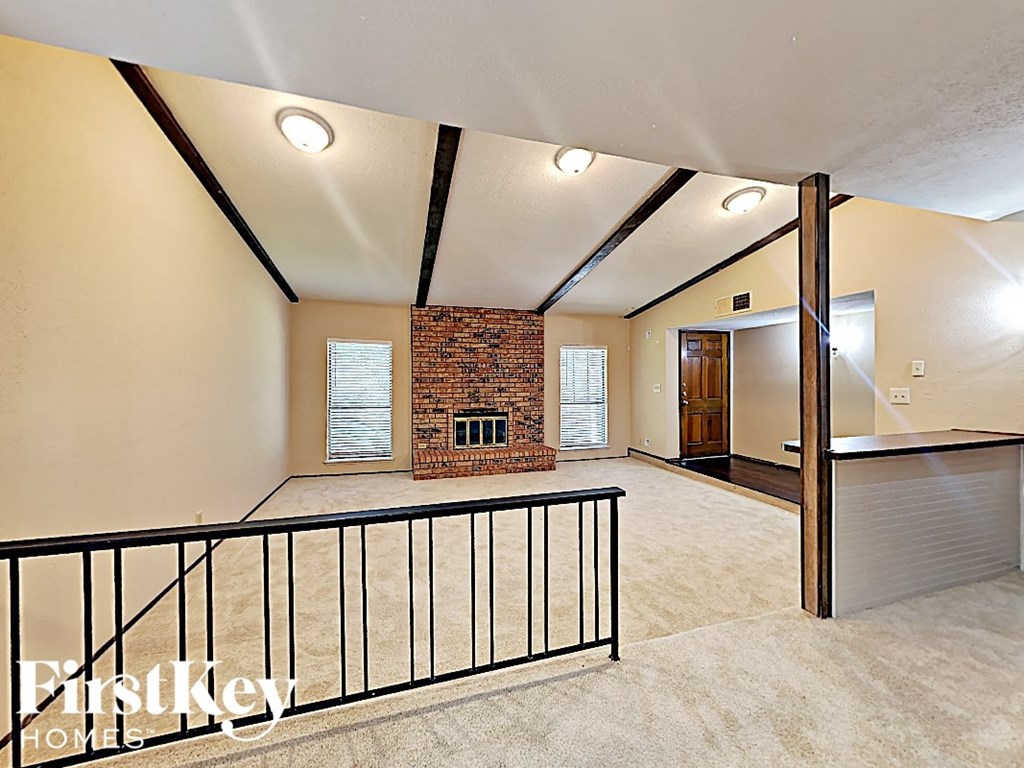 A spacious room with a brick fireplace and a balcony with a black railing.