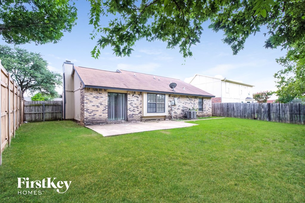 a small brick house in a backyard with a lawn and a fence