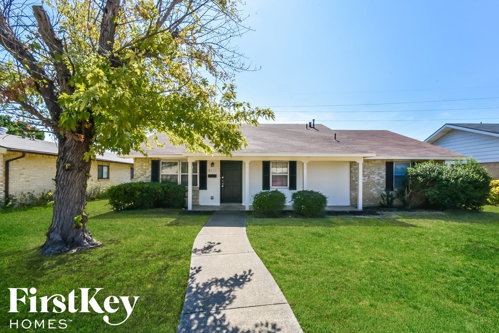 a white house with a tree in the yard and a sidewalk