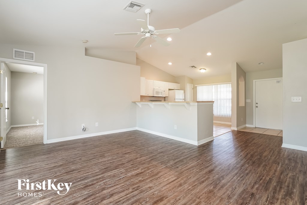 an empty living room with a kitchen and a ceiling fan