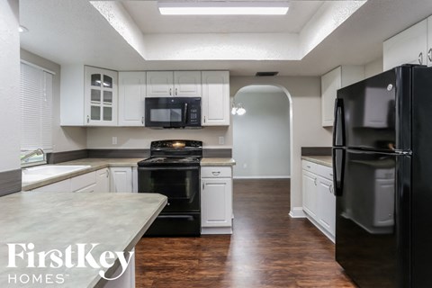 A kitchen with a black refrigerator and white cabinets.