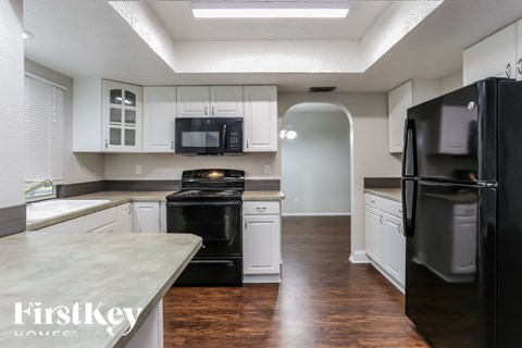 A kitchen with a black refrigerator and white cabinets.