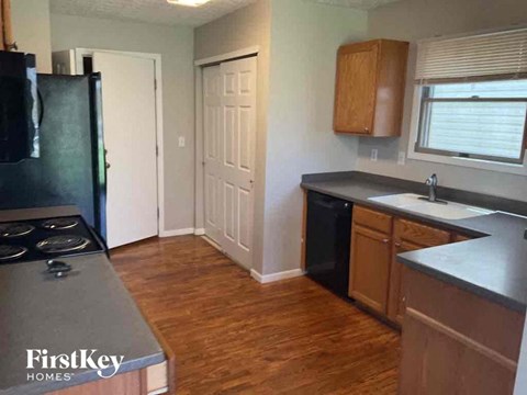 A kitchen with a black fridge, wooden floors, and a window with blinds.