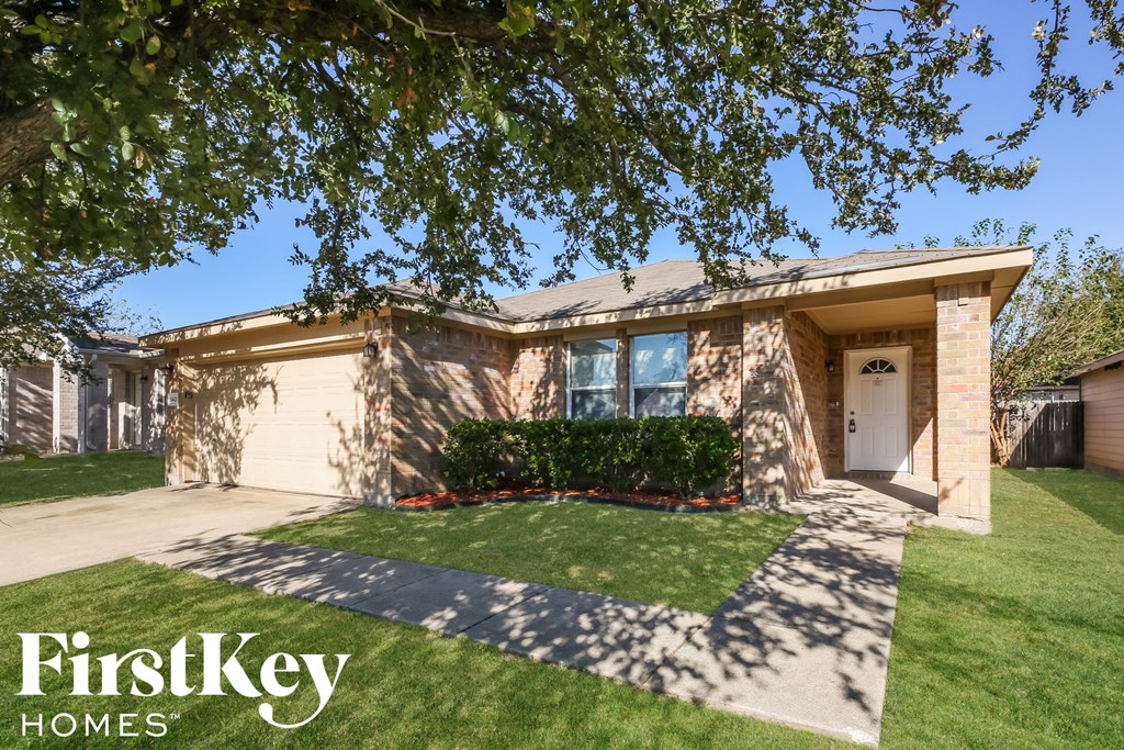 a tan brick house with a driveway and grass