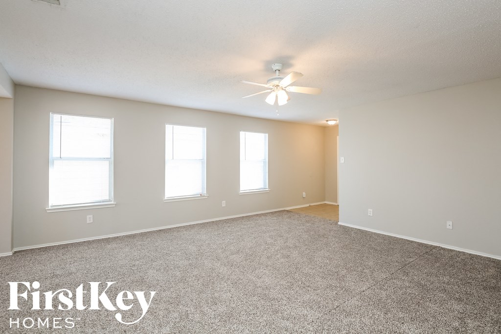 an empty living room with a ceiling fan and three windows