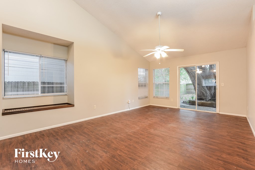 an empty living room with a window and a ceiling fan