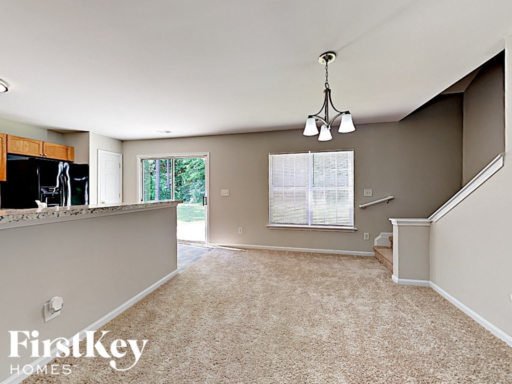 an empty living room with a kitchen and a chandelier