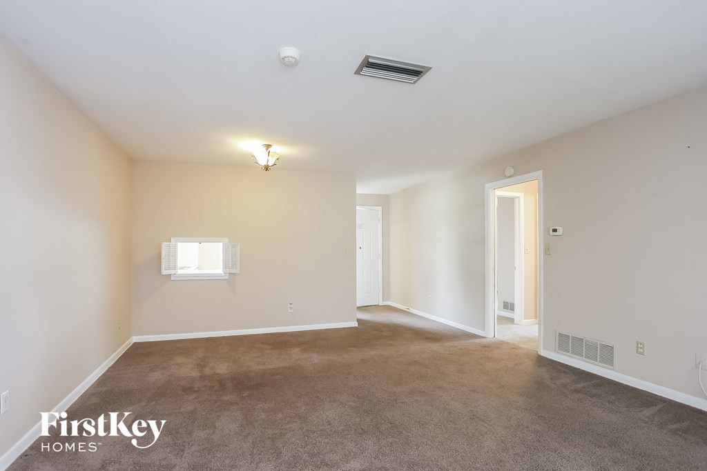 A spacious empty room with a carpeted floor and a window.