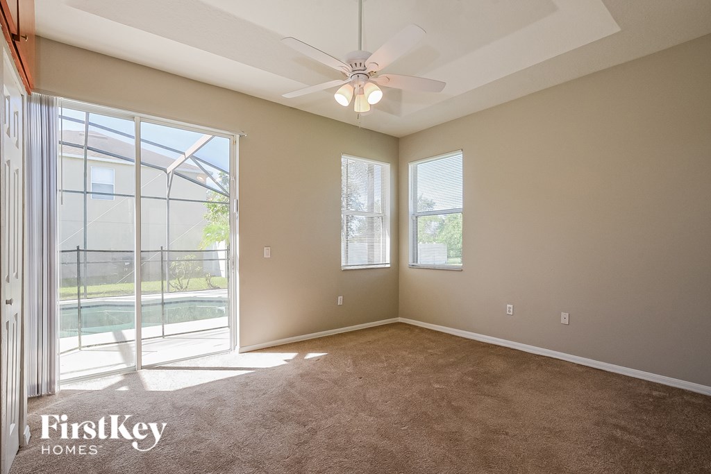 A spacious room with a ceiling fan and a view of a pool through a sliding glass door.