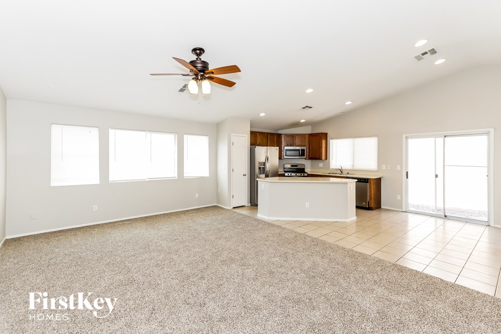 A spacious living room with a ceiling fan and a kitchen area in the background.