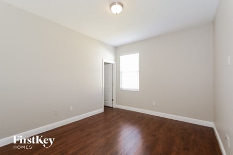 a bedroom with white walls and wood flooring and a window