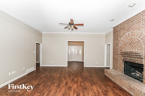 A spacious living room with a brick fireplace and a ceiling fan.