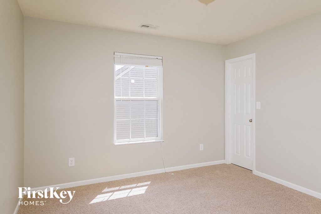 a bedroom with beige carpet and a window and a white door