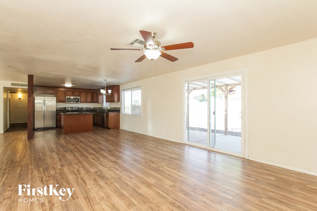 an empty living room with a ceiling fan and a kitchen